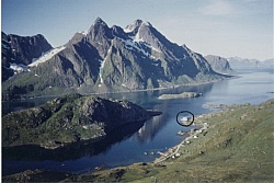 The mighty sea alpine mountains Himmeltindene and the fjord area with the white seahouse Johluns marked with a circle.